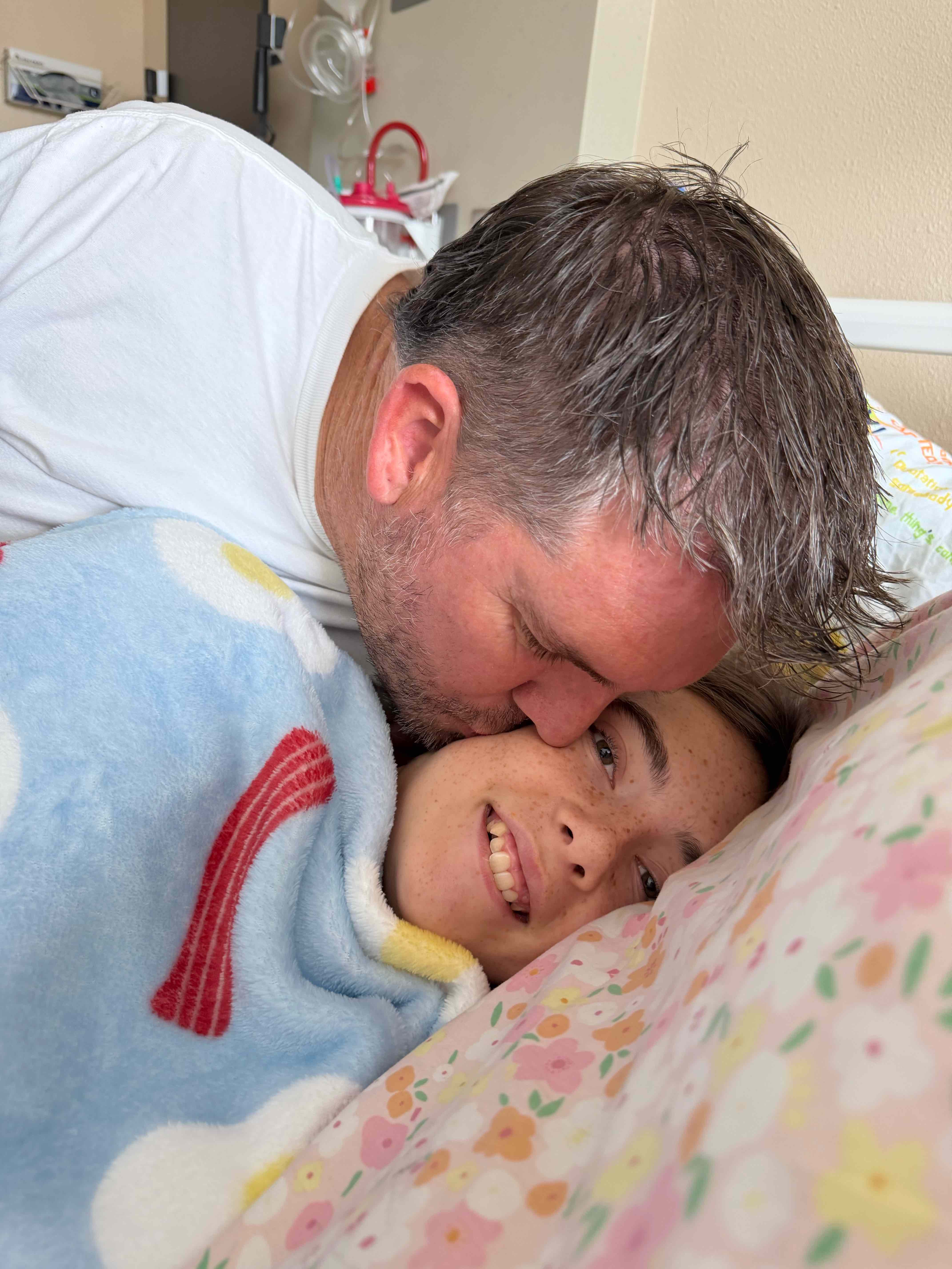 Sailor smiling as her dad gently kisses her forehead in the hospital